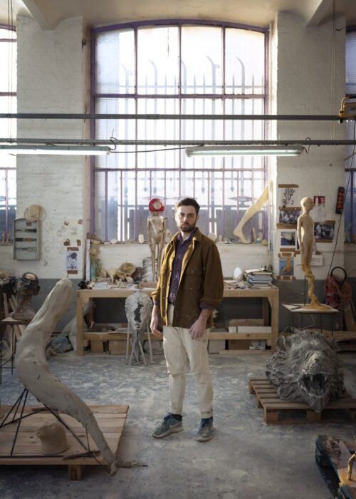 A bearded white man standing in the center of an art studio